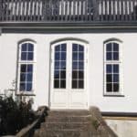 Sommerlig hvid dobbeltdør med vinduer til til husets facade